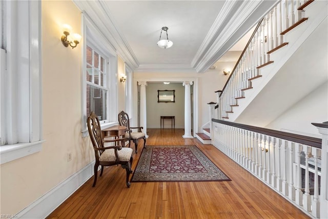 hall with baseboards, decorative columns, wood-type flooring, and ornamental molding