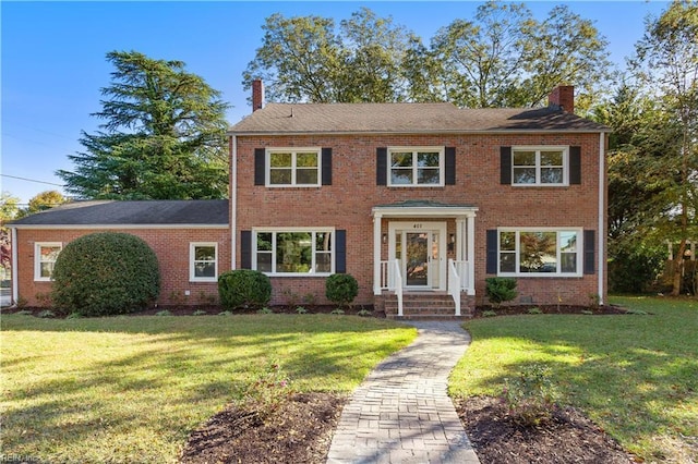 colonial home featuring brick siding, a chimney, and a front yard