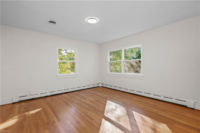 unfurnished room with wood finished floors, visible vents, a wealth of natural light, and a baseboard radiator