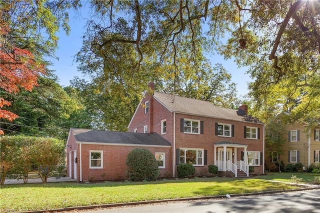 colonial home featuring a front lawn, an attached garage, brick siding, and a chimney