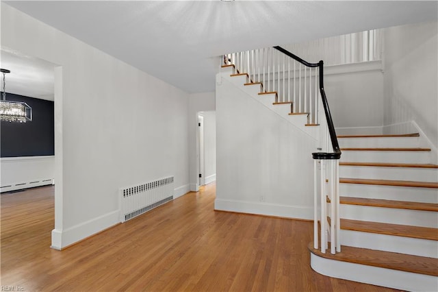 staircase with a baseboard heating unit, baseboards, radiator, and wood finished floors