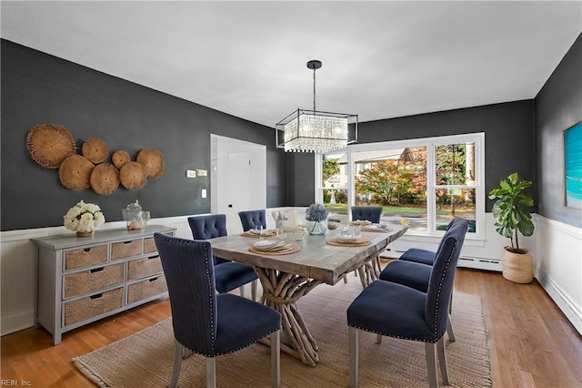 dining space with baseboard heating, a notable chandelier, light wood finished floors, and wainscoting