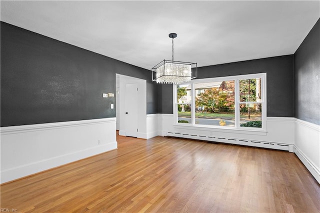 unfurnished dining area featuring an inviting chandelier, wood finished floors, wainscoting, and a baseboard radiator