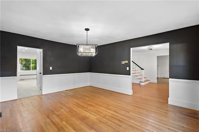 spare room with a wainscoted wall, stairs, radiator heating unit, and light wood-style floors