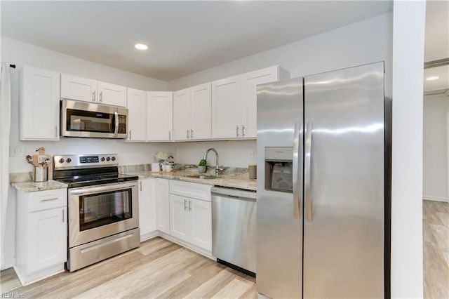 kitchen with light wood-type flooring, a sink, light stone counters, white cabinetry, and stainless steel appliances