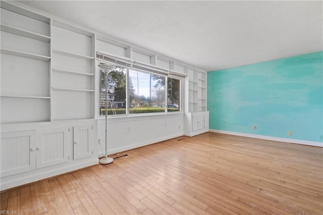 empty room with baseboards, built in shelves, and hardwood / wood-style flooring