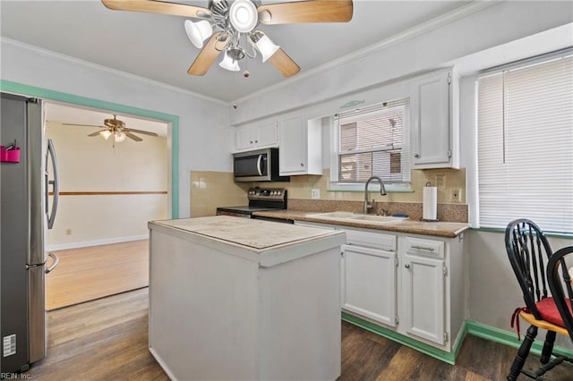 kitchen with a sink, ornamental molding, dark wood-type flooring, stainless steel appliances, and white cabinetry