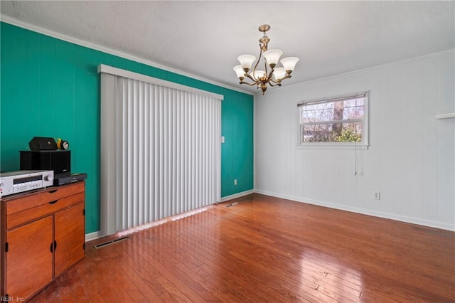 spare room with visible vents, baseboards, a chandelier, ornamental molding, and hardwood / wood-style flooring