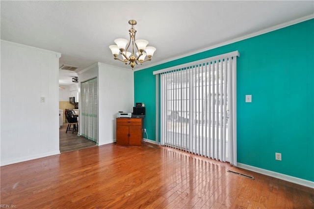 unfurnished room with visible vents, a notable chandelier, ornamental molding, wood finished floors, and baseboards