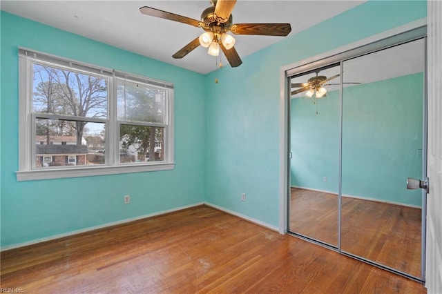 unfurnished bedroom with a ceiling fan, wood finished floors, a closet, and baseboards