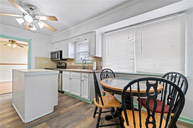 kitchen with dark wood finished floors, stainless steel appliances, white cabinetry, crown molding, and a center island