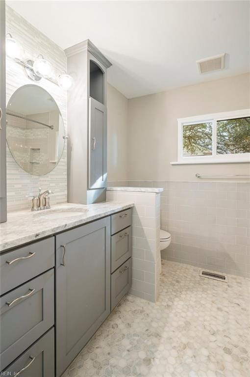 bathroom featuring tile walls, visible vents, toilet, and vanity