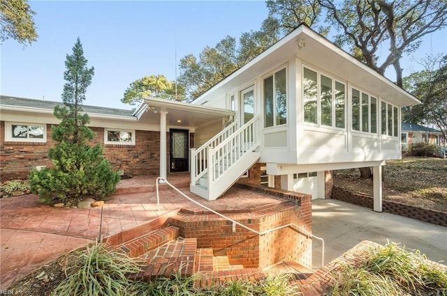 back of property with brick siding, concrete driveway, an attached garage, and a sunroom