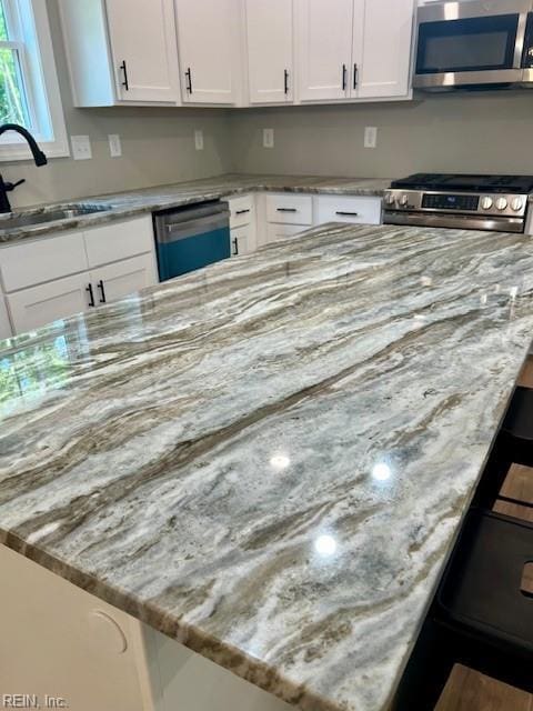 kitchen featuring a kitchen bar, a sink, light stone counters, stainless steel appliances, and white cabinets