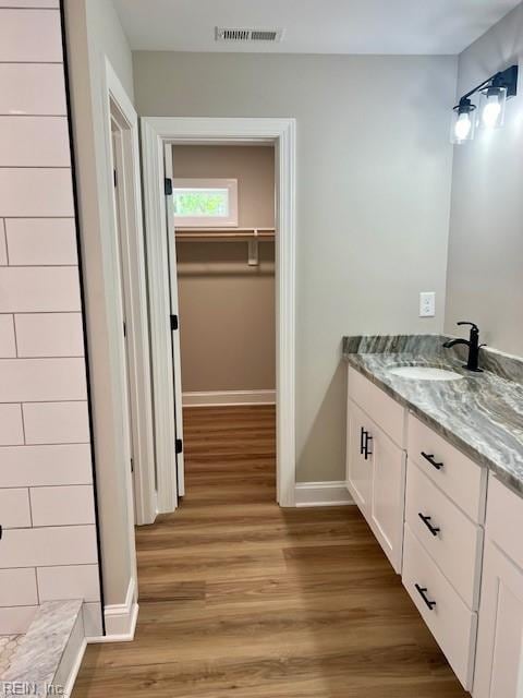 full bath with visible vents, a walk in closet, baseboards, wood finished floors, and vanity