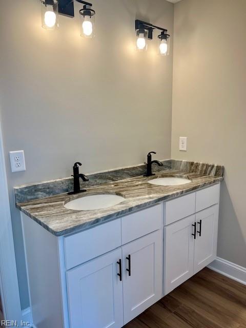 bathroom with double vanity, wood finished floors, baseboards, and a sink