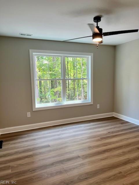 empty room with visible vents, ceiling fan, baseboards, and wood finished floors