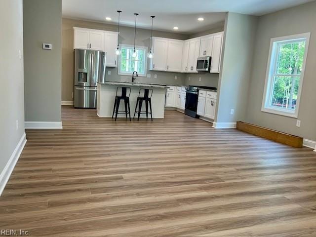 kitchen featuring stainless steel appliances, a kitchen bar, open floor plan, and white cabinetry