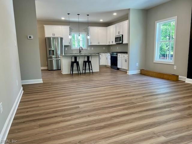 kitchen with open floor plan, appliances with stainless steel finishes, white cabinetry, and light wood-style floors