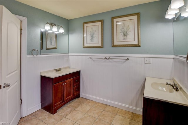 bathroom featuring tile patterned flooring, two vanities, a wainscoted wall, and a sink