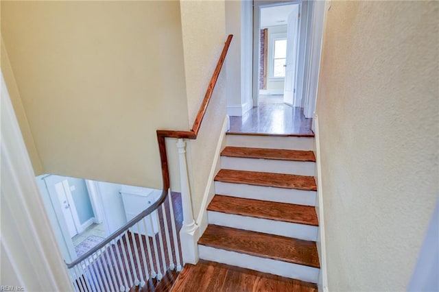 stairs with wood finished floors and a textured wall