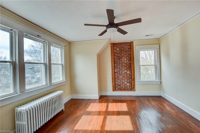 spare room featuring a healthy amount of sunlight, wood finished floors, and radiator heating unit