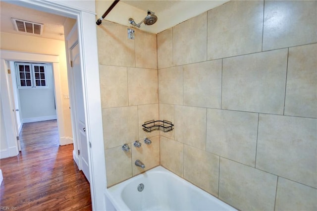 full bath with baseboards, wood finished floors, visible vents, and shower / bath combination