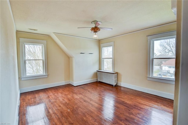 additional living space with a wealth of natural light, radiator heating unit, a ceiling fan, and wood finished floors