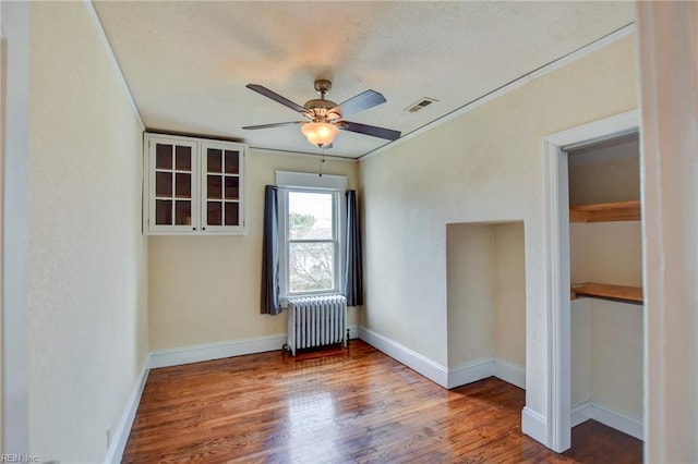 spare room with radiator, wood finished floors, baseboards, visible vents, and ceiling fan