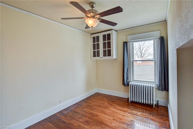 spare room featuring ornamental molding, radiator, baseboards, and wood finished floors