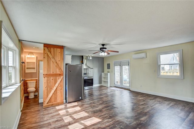 unfurnished living room with a barn door, wood finished floors, french doors, and a wall unit AC