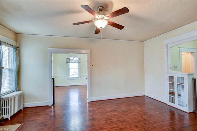 empty room with ceiling fan with notable chandelier, radiator, wood finished floors, and baseboards