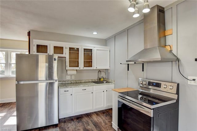 kitchen with a sink, appliances with stainless steel finishes, white cabinets, wall chimney exhaust hood, and dark wood-style flooring