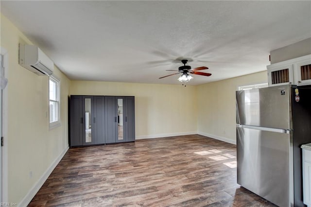 kitchen featuring a wall unit AC, a ceiling fan, baseboards, dark wood finished floors, and freestanding refrigerator