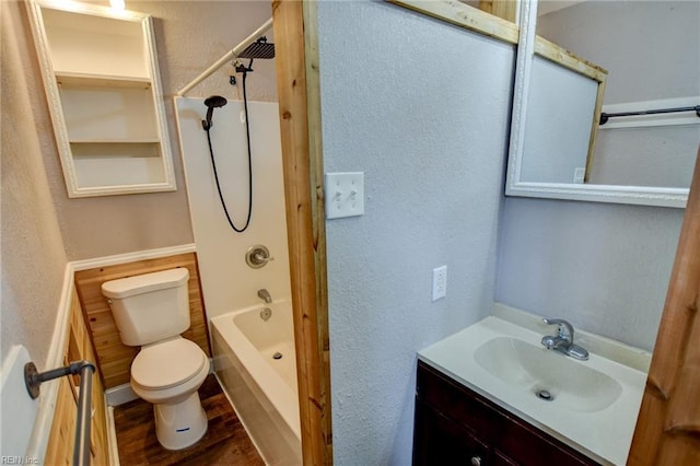 bathroom with toilet, shower / bathtub combination, wood finished floors, vanity, and a textured wall