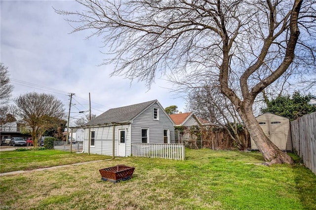 exterior space with a fire pit, a lawn, a fenced backyard, an outbuilding, and a storage unit