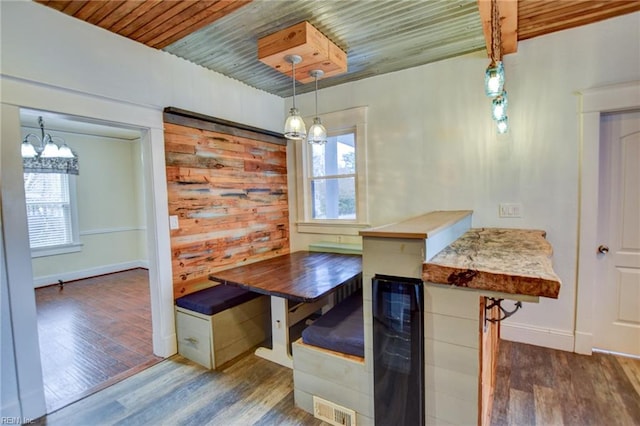 unfurnished dining area with beverage cooler, wood finished floors, breakfast area, an inviting chandelier, and wood ceiling