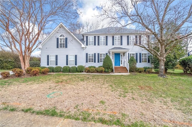 colonial home featuring roof with shingles and a front yard