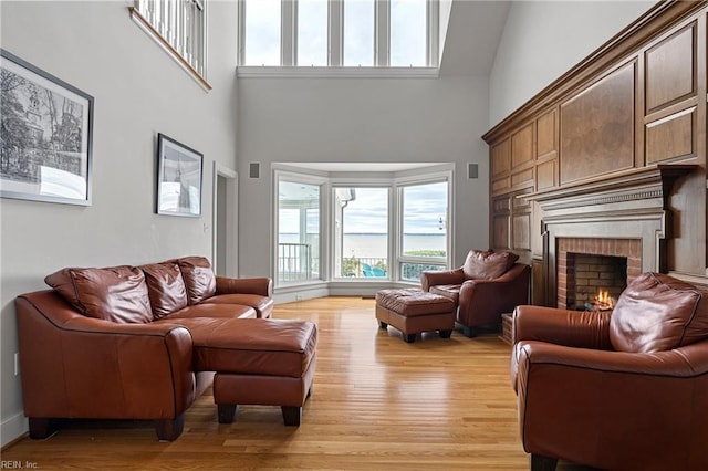 living room with light wood finished floors, a brick fireplace, and a towering ceiling