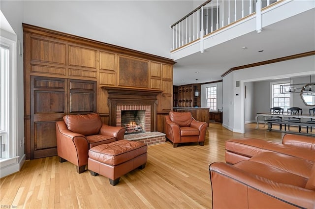 living area with light wood finished floors, a brick fireplace, crown molding, and baseboards