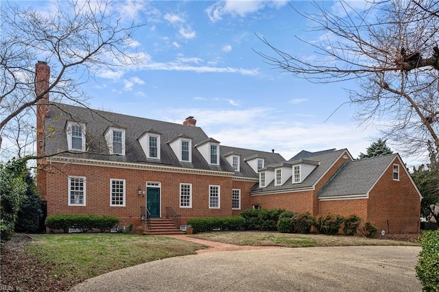 view of front of home featuring brick siding, a chimney, a front yard, and a shingled roof