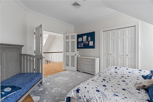 bedroom with wood finished floors, visible vents, a closet, and ornamental molding