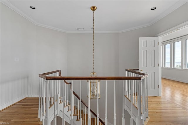 corridor featuring an upstairs landing, visible vents, light wood finished floors, and ornamental molding