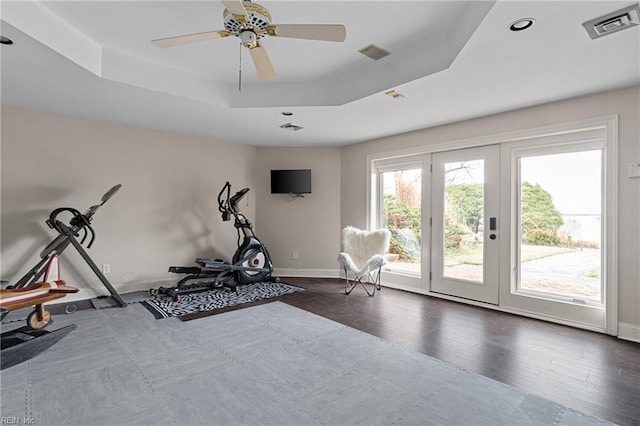 exercise room featuring visible vents, baseboards, a tray ceiling, wood finished floors, and a ceiling fan