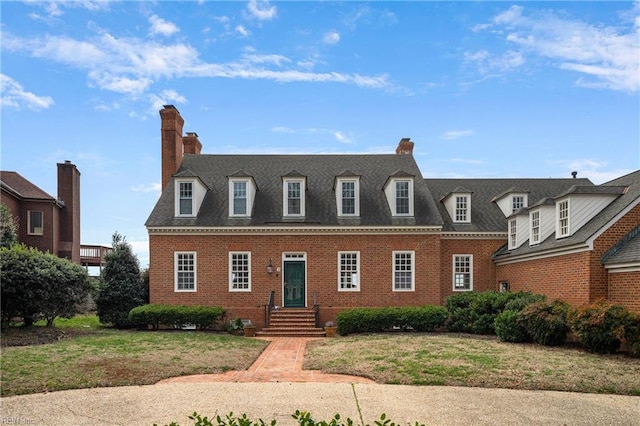 view of front of house featuring brick siding, a chimney, and a front lawn