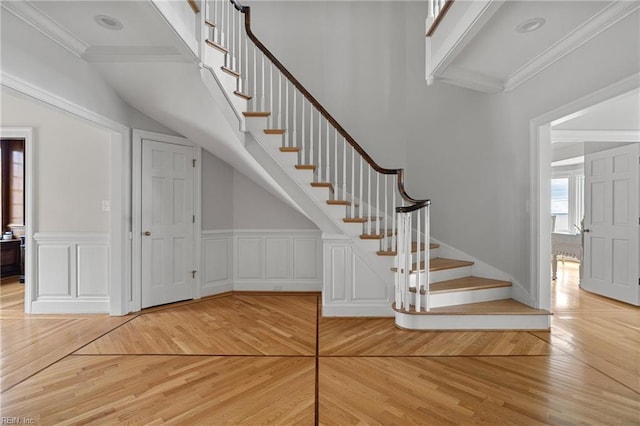 stairway with a decorative wall, wood finished floors, and ornamental molding