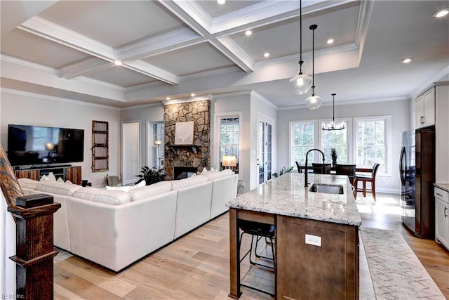 living area featuring light wood finished floors, beamed ceiling, ornamental molding, a fireplace, and coffered ceiling