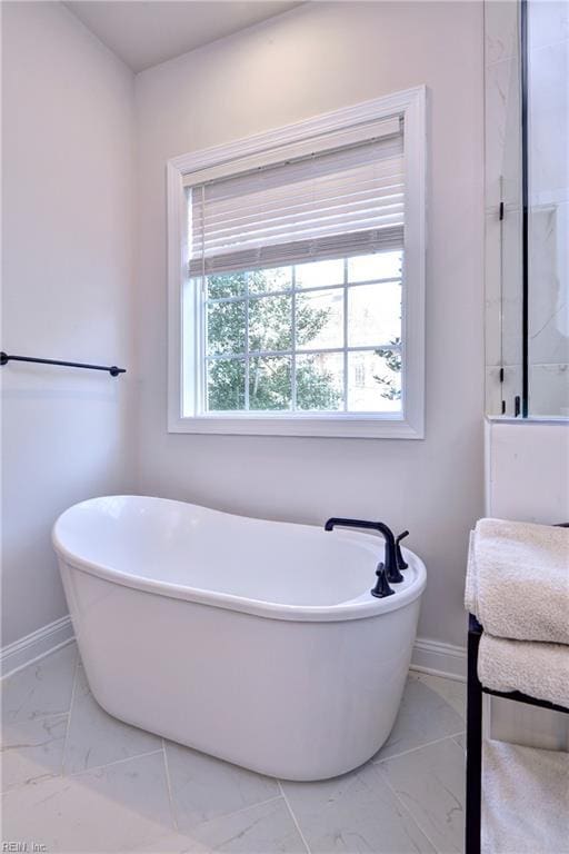 full bathroom featuring a freestanding tub, baseboards, and marble finish floor