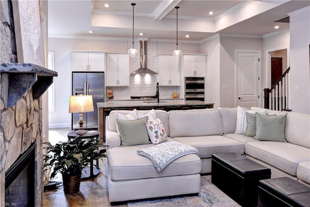 living room featuring baseboards, recessed lighting, ornamental molding, a stone fireplace, and stairs