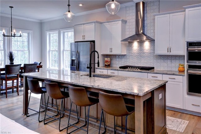 kitchen with ornamental molding, a sink, appliances with stainless steel finishes, wall chimney range hood, and decorative backsplash